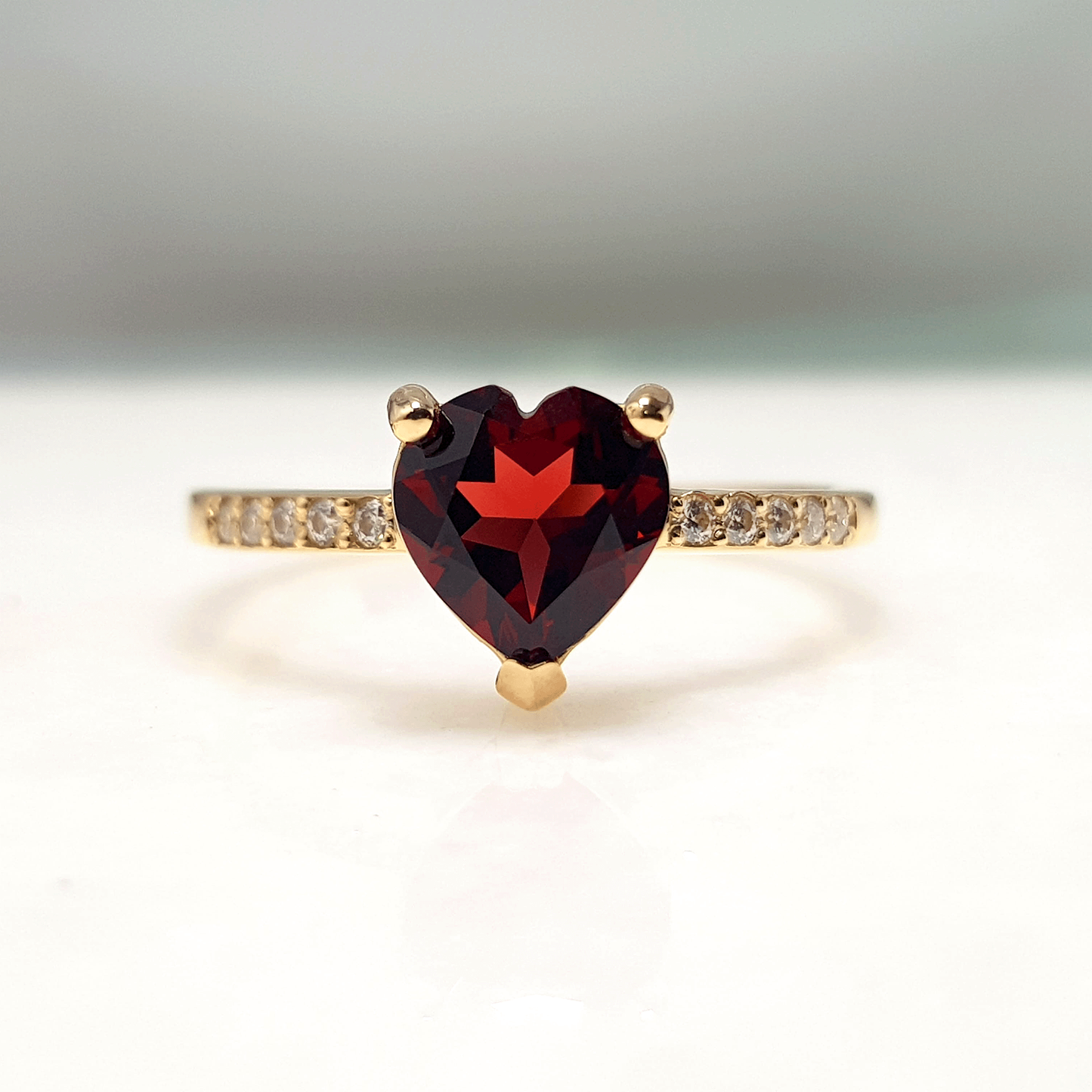 Hermoza Sortija con un Granate color Rojo profundo en el centro. Esta gema tiene forma de Corazón. Además cuenta con 5 Moissanitas en cada lado
